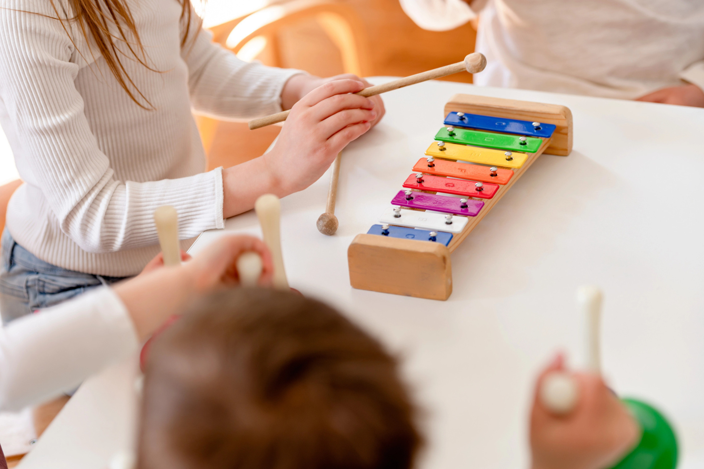 dreieins Innovative Pädagogik – dreieins Kreativitätsbereich Musikalisches Gestalten: Zu sehen ist ein Tisch, auf dem ein Xylophon steht und Kinder, die darum sitzen.