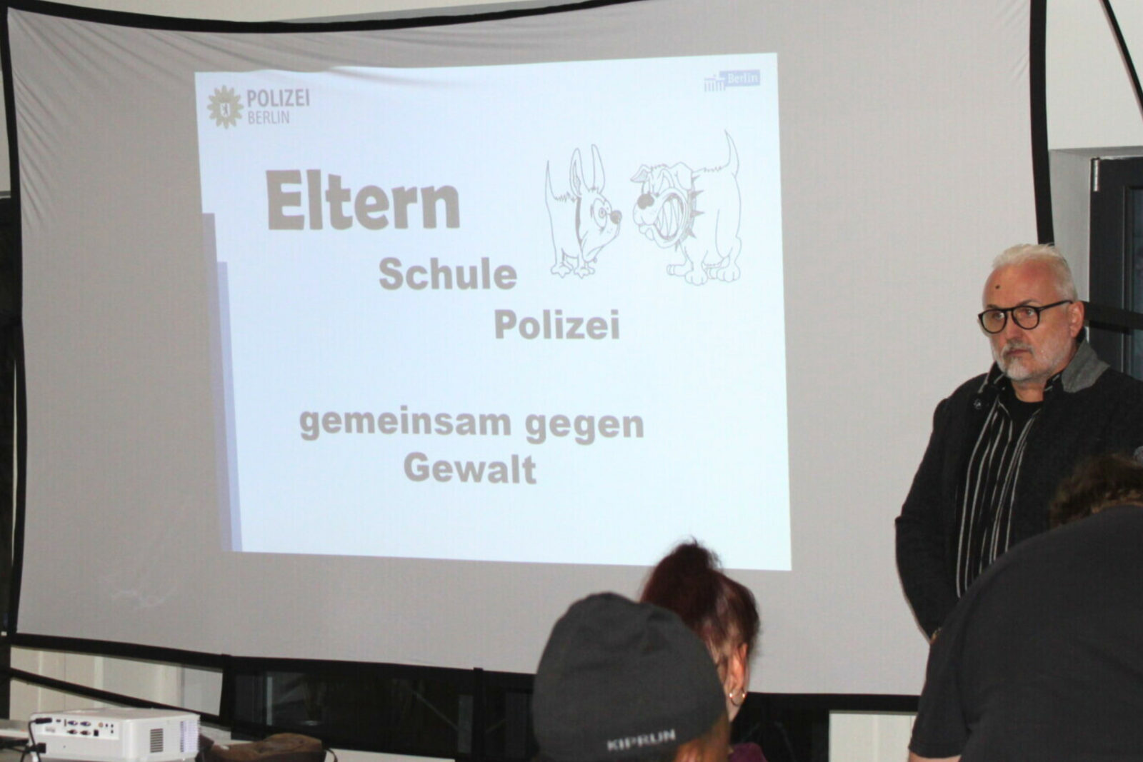 Elternabend zum Thema Gewaltprävention: Abgebildet ist eine Leinwand, auf die Präsentation der Veranstaltung gezigt wird sowie verschiedene Menschen.