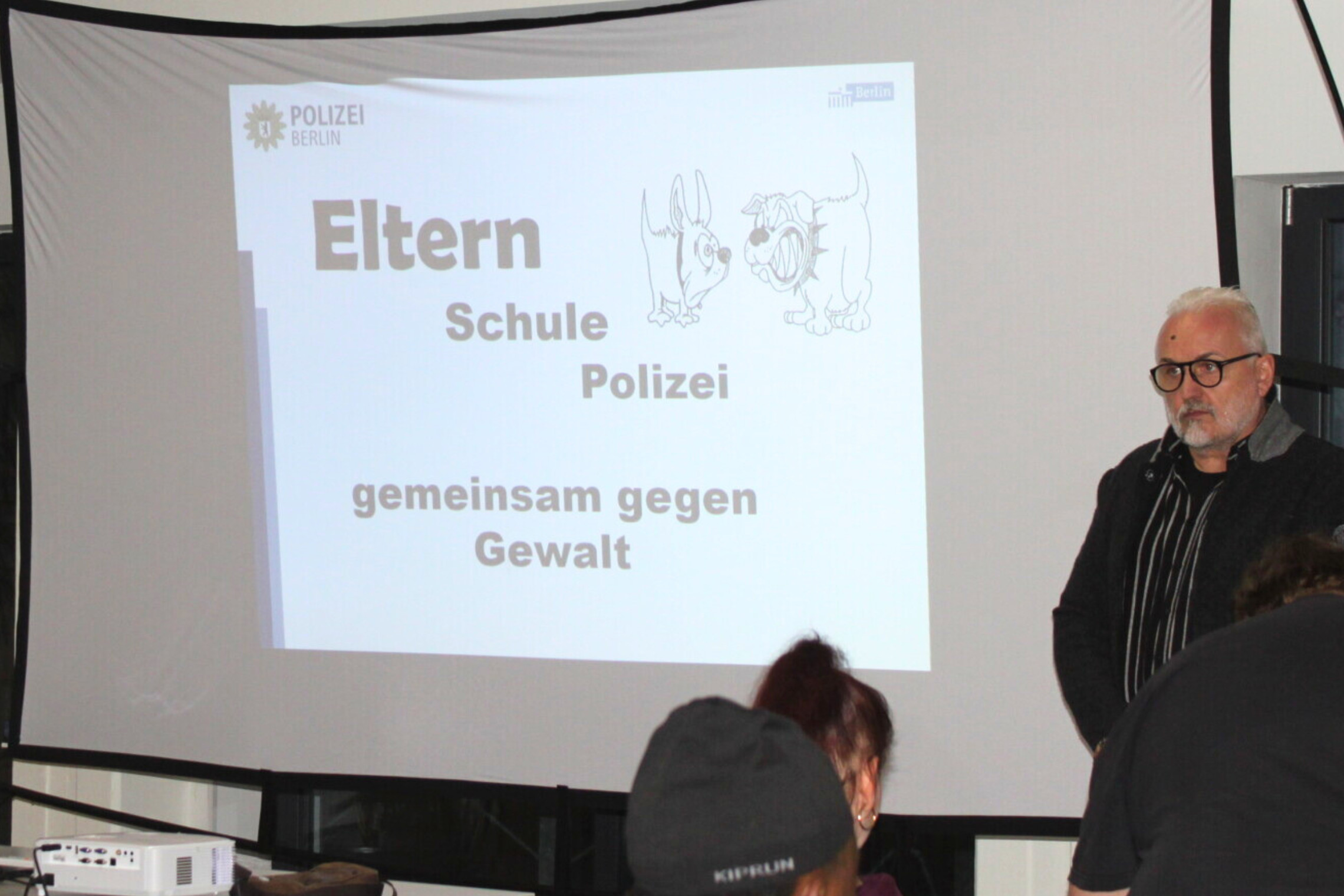 Elternabend zum Thema Gewaltprävention: Abgebildet ist eine Leinwand, auf die Präsentation der Veranstaltung gezigt wird sowie verschiedene Menschen.