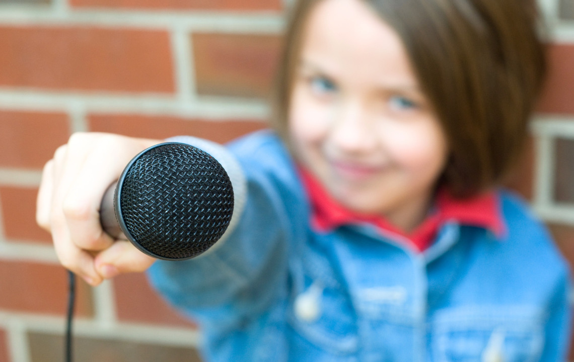 dreieins bilinguale Kindertagesstätte Berlin-Kaulsdorf - Medienprojekt Podcast: Abgebildet ist ein Kind, das ein Mikrofon in der Hand hält.