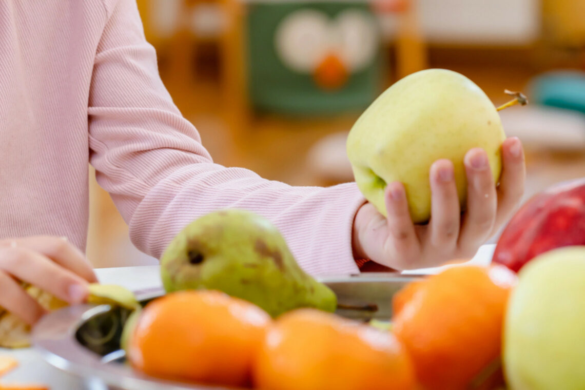 dreieins Innovative Pädagogik – dreieins Gesunde Ernährung Obstpause: Ein Kind hält in der Hand einen Apfel.